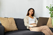 © LIGHTFIELD STUDIOS - A woman sits comfortably on a sofa, focused on her laptop, enjoying a moment of productivity.