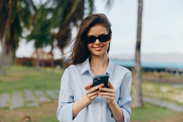 Canvas Print - Woman, sunglasses, palm tree, cell phone, smile a woman in sunglasses holds a cell phone and smiles while standing in front of a palm tree, capturing a moment of tropical relaxation