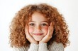 © Attasit - Young girl with curly hair smiling brightly and looking directly at the camera with her hands resting on her cheeks Isolated on white background