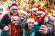 © charmedlightph - Self portrait of young people wearing santa claus hat celebrating Christmas day outside - Happy multiracial friends group taking selfie under tree having xmas holiday party - Winter holidays concept