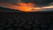 © Rohit k  - Intense orange sunset casting a warm glow over a vast, cracked and barren landscape, with distant mountains silhouetted against the colorful sky