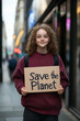 © Rohit k  - Student holding up save the planet poster and smiling at climate change protest in urban area, supporting environmental protection