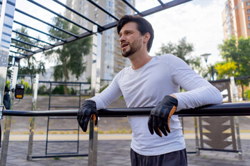 on the street in the park near the horizontal bars a handsome brunette guy in black shorts and white T-shirts is resting near the horizontal bar after workout healthy lifestyle