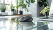 © Itsaraporn - Close-up of a wireless mouse beside a laptop on a glass desk, with office plants and files in the background