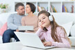 © aletia2011 - Cheerful little girl using a laptop at home with her parents in the background.