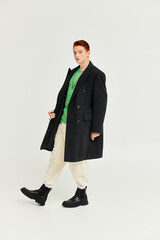 A young man with striking red hair showcases his fashion sense in an elegant winter coat and stylish boots.