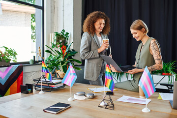 Two coworkers engage enthusiastically while discussing work amid vibrant LGBT decorations.