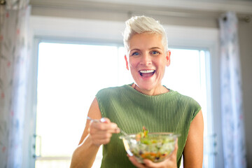 Mature smiling woman eating salad, fruits and vegetables.