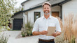 © VERTEX SPACE - A smiling man stands outside modern home, holding document. His cheerful expression reflects confidence and positivity, surrounded by greenery and stylish landscaping