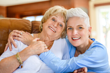 Happy daughter embracing from behind elderly mother at living room. Love and care.