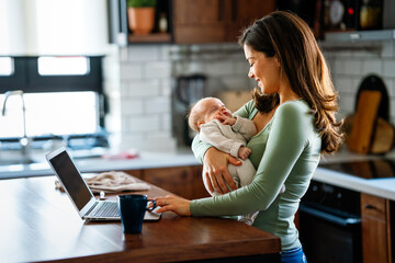 Wall Mural - Stay at home mom working remotely on laptop while taking care of her baby.