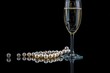 © volga - Elegant champagne glass with pearls on black background