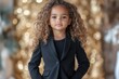 © SerPak - A three year old girl with voluminous curls confidently poses in a fitted black pantsuit and stylish ankle boots. She holds imaginary glasses against a shimmering gold backdrop, embodying playful eleg