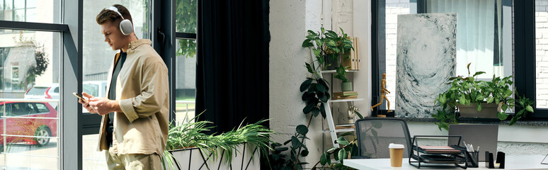 A determined young professional engages with his phone in a stylish office filled with greenery.