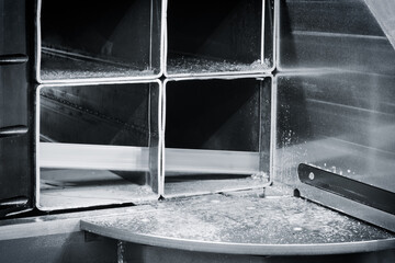 Poster - A machine is cutting metal into pieces. The machine is black and silver. The metal pieces are being cut into small squares
