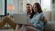 © Yuliia - Happy young couple using laptop for ecommerce doing online shopping with shop app together at home Caucasian man and woman looking at computer buying searching in internet booking trip tickets choose