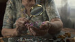 © diablosiatr - Elderly woman examining raw crystal quartz beads through magnifying glass.