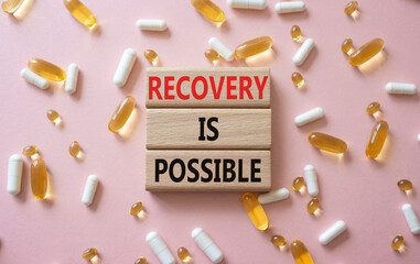 Recovery is possible symbol. Concept words Recovery is possible on wooden blocks. Beautiful pink background with pills. Healthcare and Recovery is possible concept. Copy space.