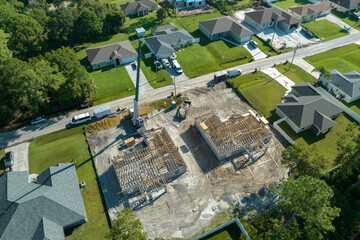 Wall Mural - Aerial view of lifting crane and builders working on unfinished residential house with wooden roof frame structure under construction in Florida suburban area