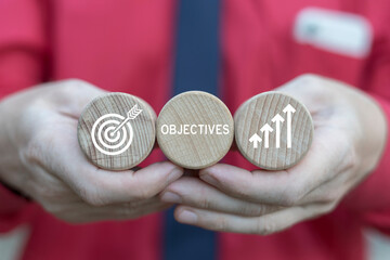 Businessman holding wooden blocks sees word: OBJECTIVES. Company target achievement, business goal or objective to achieve, team strategy, leadership development, aiming for winning goal concept.