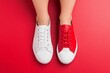 © Natalia - A person showcases mismatched red and white shoes on a vibrant red background for unique self-expression