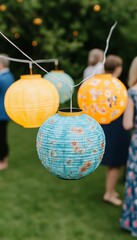 Wall Mural - Three colorful paper lanterns hanging in a garden, with blurred people in the background.