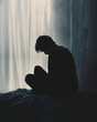 © Zita Stankova - Silhouette of a man in a dark room stiting on a bed in sadness.