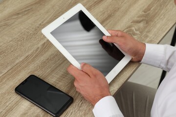 Businessman with tablet and smartphone at wooden table, closeup. Modern technology