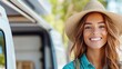 © Pinklife - A woman in a brimmed hat smiles joyfully with a blurred camper van in the background, symbolizing a carefree travel lifestyle in an outdoor setting.