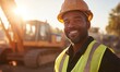 © Galina - A construction worker wearing a hard hat and safety vest smiles at the camera. He is standing in front of a large construction vehicle, with the sun shining brightly in the background