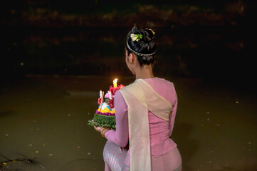 Back view Thai woman in traditional costume holding floating Kratong with candle ready to release in the river during Loi Kratong festival