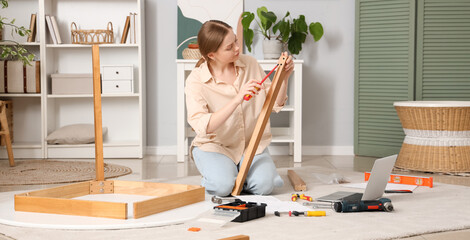 Beautiful young woman with screwdriver assembling table at home