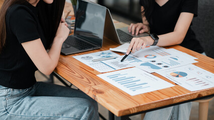 Wall Mural - two women discussing financial data with laptops and printed charts, showcasing teamwork and busines