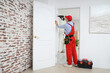 © Pixel-Shot - Male worker with electric drill installing door hinge at home