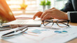 © นิโลบล ชํานาญธรรม - Businessman reviewing financial reports with laptop, glasses, and documents, showcasing professional workspace filled with charts and graphs