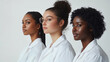 © Phuwadon - Three diverse women in white lab coats standing in profile, showcasing unity and professionalism against a neutral background.