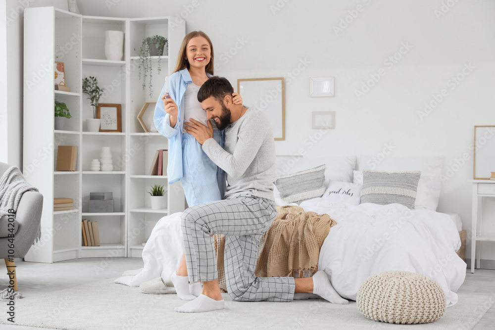 Happy young couple with pregnancy test hugging in bedroom