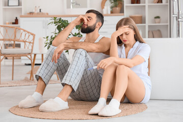 Wall Mural - Upset young couple with pregnancy test sitting on floor in bathroom