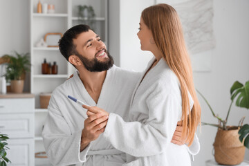 Wall Mural - Happy young couple with pregnancy test hugging in bathroom