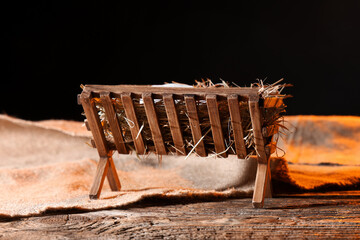 Manger with baby Jesus and cloth on table against dark background