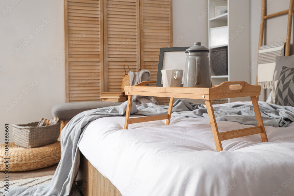 Tray with kettle, cup of coffee and frame on bed in bedroom