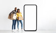 © Prostock-studio - A joyful black couple stands together, holding cardboard boxes. They are positioned beside a large empty phone frame, creating a playful atmosphere. Their smiles reflect excitement and teamwork.