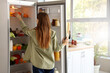 © Pixel-Shot - Young woman taking pumpkin from open fridge in kitchen