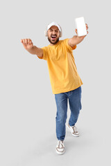 Wall Mural - happy young man in headphones with blank mobile phone singing on light background