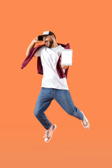 Wall Mural - Young man with blank tablet computer jumping on orange background