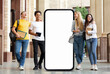 © Prostock-studio - A group of four students enjoys a lighthearted moment outside a university building, passing by huge phone with blank screen