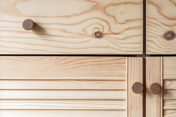 Wooden louvered doors with wooden knob handles close-up. Louvered doors of outdoor kitchen are made from light pine wood with natural grain pattern