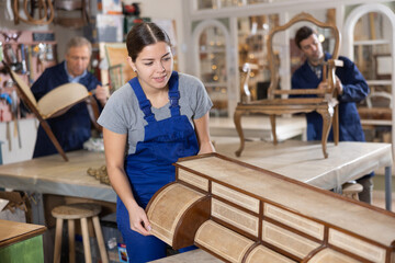 Woman restorer carefully and carefully restores chest of drawers in a restoration workshop