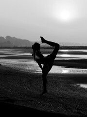 silhouette of a girl doing gymnastics on the beach by the sea with one leg in black and white effect