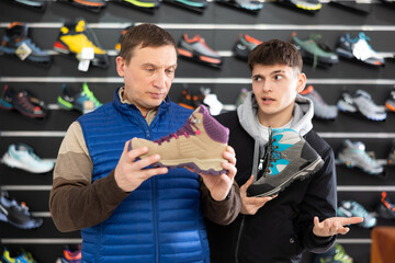 Father and son together choose and buy winter sports shoes for hiking in a sports store